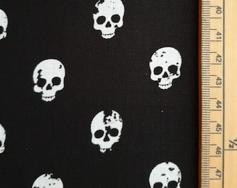 May include: Black fabric with a repeating pattern of white skulls. The skulls are stylized with varying levels of detail. A wooden ruler with inch markings is visible along the right edge of the fabric.