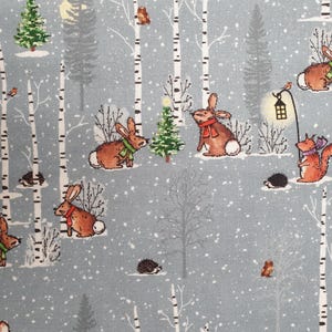 Peut inclure: Tissu bleu clair avec un motif de forêt hivernale. Des lapins avec des écharpes, un écureuil avec une lanterne et d'autres animaux sont représentés parmi les arbres enneigés. Ambiance festive et hivernale.