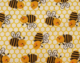 May include: A fabric with a repeating pattern of cartoon bees and honeycomb. The bees are yellow and black with white wings and small antennae. The honeycomb background is yellow, and the fabric is off-white.