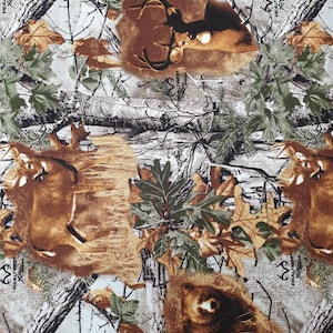 Op de afbeelding: Camouflage stof met herten, beren en bladeren in bruin, groen en wit. Het patroon bevat herten met geweien, beren en bladeren, wat een bos thema creëert. De stof heeft een getextureerde uitstraling.