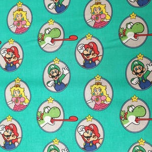 Könnte beinhalten: Türkisfarbener Stoff mit einem sich wiederholenden Muster aus kreisförmigen Illustrationen von Mario, Luigi, Prinzessin Peach und Yoshi. Jede Figur ist von einem grauen Oval und einem goldenen Stern umrahmt. Die Charaktere tragen ihre typischen Outfits.