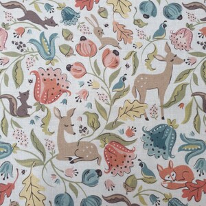 Könnte beinhalten: Ein weißer Stoff mit einem sich wiederholenden Muster aus Waldtieren wie Hirschen, Füchsen und Eichhörnchen, durchsetzt mit floralen Elementen, Eichenblättern und Eicheln in gedämpften Orange-, Salbeigrün- und Staubblautönen.