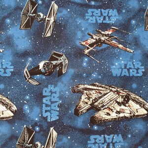 Op de afbeelding: Een blauwe stof met een herhalend patroon van Star Wars-ruimteschepen, waaronder de Millennium Falcon, X-wing-jagers en TIE-jagers tegen een sterrenhemel-achtergrond met het Star Wars-logo in lichtblauwe tekst over het hele oppervlak.