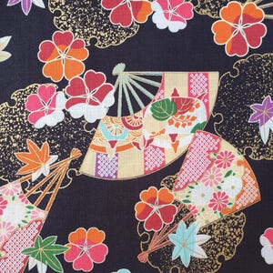 May include: A black fabric featuring a repeating pattern of folding fans and various flowers including orange, pink, and light blue blossoms. The design incorporates gold-colored accents and maple leaves in shades of green, orange, and purple.