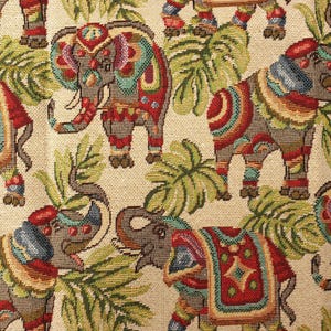 May include: A woven fabric featuring a repeating pattern of elephants in shades of red, blue, and green against a beige background. The elephants are decorated with ornate, colorful blankets and are interspersed with green palm leaf motifs.
