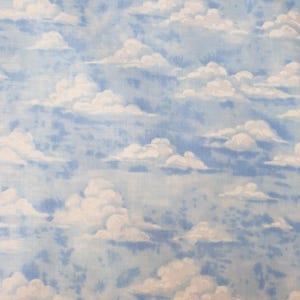 May include: A fabric featuring a repeating pattern of white, fluffy clouds set against a light blue sky background. The design displays a soft, painterly texture with varying shades of blue, creating a sky-like appearance across the textile surface.