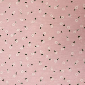 Puede incluir: Una tela rosa con un patrón floral blanco. La tela tiene una textura sutil y un diseño delicado.