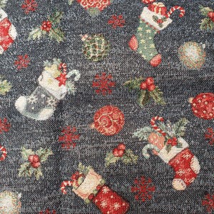 Può includere: Un tessuto blu scuro con un motivo natalizio ripetuto di calze rosse e verdi, ornamenti rossi, bacche di agrifoglio e fiocchi di neve. Il tessuto intrecciato mostra una superficie strutturata con dettagliati motivi festivi sullo sfondo scuro.