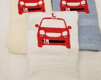 May include: Three white towels with red embroidered cars on them. The cars have a red 'L' on the roof, indicating a learner driver.