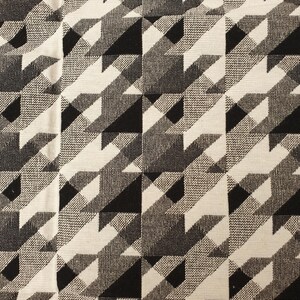 Puede incluir: Una tela tejida con un patrón repetitivo de pata de gallo en tonos contrastantes de negro, blanco y gris. El diseño consiste en formas geométricas entrelazadas que crean una textura visual nítida, angular y rítmica en toda la superficie.