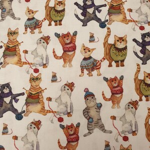 Könnte beinhalten: Ein weißer Stoff mit einem sich wiederholenden Muster aus verschiedenen Katzen, die bunte Strickpullover, Mützen und Schals tragen. Einige Katzen spielen mit roten Wollknäueln, während andere mit Nadeln stricken.