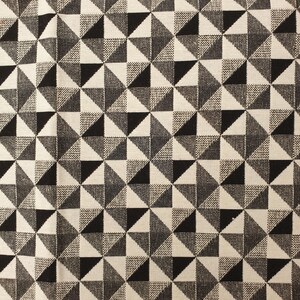 Puede incluir: Una tela tejida con un patrón geométrico repetitivo de cuadrados divididos en cuatro triángulos. El diseño alterna entre triángulos negros sólidos, blancos sólidos y grises texturizados, creando una cuadrícula de formas entrelazadas.