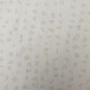 Könnte beinhalten: Ein heller, cremeweißer Stoff mit einem sich wiederholenden Muster aus kleinen, unregelmäßigen, beigefarbenen Formen, die über die Oberfläche verteilt sind. Das Textil weist eine sichtbare Webstruktur mit einer gleichmäßigen, richtungslosen Anordnung dieser sanft getönten Markierungen auf.