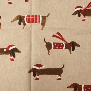 Könnte beinhalten: Ein beigefarbener Stoff mit einem sich wiederholenden Muster aus braunen Dackeln, die verschiedene rot-weiße Winteraccessoires tragen, darunter Weihnachtsmützen, Schals, Pullover mit Karomuster, Sternen oder Punkten sowie kleine rote Stiefel.