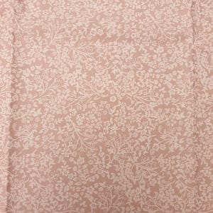 Könnte beinhalten: Nahaufnahme eines Stoffes mit sich wiederholendem Blumenmuster. Der Stoff hat einen hellrosa Hintergrund mit einem zarten, flächendeckenden Design aus kleinen weißen Blüten und dünnen, sich windenden Stielen. Das Muster ist gleichmäßig verteilt.