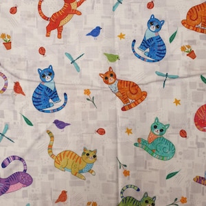 Puede incluir: Tela blanca con un estampado repetido de gatos de dibujos animados coloridos, pájaros, libélulas, mariquitas y flores en macetas. Los gatos son de varios colores, incluyendo naranja, azul, verde y amarillo. La tela tiene un diseño caprichoso y juguetón.