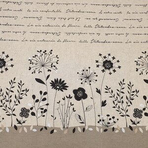 Op de afbeelding: Een beige stof met een zwart-wit bloemenpatroon. De stof heeft een herhalend patroon van gestileerde bloemen en bladeren. De stof heeft een textuur en een subtiele glans.