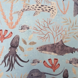 Puede incluir: Tela azul claro con un diseño submarino. Presenta un tiburón martillo, un tiburón, calamares, rayas y peces, junto con coral y algas marinas. Las ilustraciones son en tonos grises, marrones y rojos.