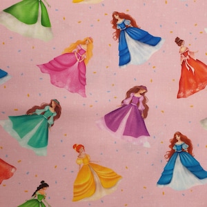 Op de afbeelding: Roze stof met illustraties van prinsessen in kleurrijke jurken. De prinsessen hebben lang haar en zijn verspreid over de stof. De stof heeft ook kleine confetti-achtige details.