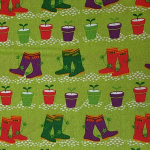 May include: A green fabric with a repeating pattern of red and green rain boots and small potted plants with green leaves. The plants are in pots of red, green, and purple.