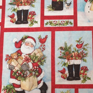 May include: A cotton fabric panel featuring a Christmas theme with rectangular illustrations of Santa Claus, black boots filled with holiday greenery, gingerbread cookies, wrapped gifts, red cardinals, and holly on a light blue background.