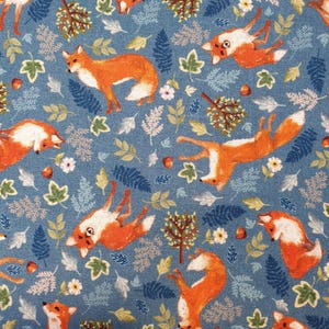 May include: A blue fabric featuring a repeating pattern of orange foxes, small green and white trees, various fern-like leaves, small white flowers, and brown acorns scattered across the surface in a dense, multi-directional arrangement.