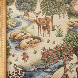 Könnte beinhalten: Ein Wandteppichstoff mit beigefarbenem Hintergrund, der einen Bach, Bäume und Hirsche zeigt. Der Bach ist blau und grün mit braunen Steinen. Die Bäume sind grün mit braunen Stämmen. Die Hirsche sind braun mit weißen Flecken. Der Stoff hat eine gewebte Textur.