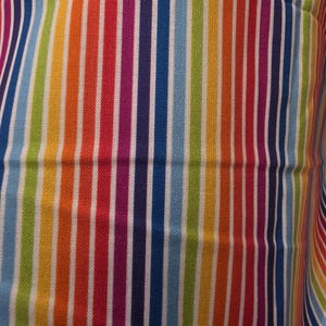 Puede incluir: Primer plano de una tela con rayas verticales en colores del arcoíris. Las rayas alternan entre tonos vibrantes de rojo, naranja, amarillo, verde, azul y morado, separadas por finas líneas blancas. La tela parece estar tejida apretadamente.