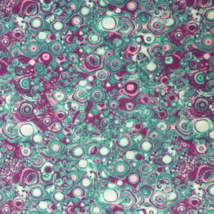 以下が含まれることがあります： ターコイズ、パープル、ホワイトの渦巻き模様の抽象的な生地。模様はマーブル模様に似ています。