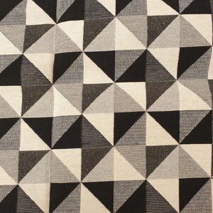 Puede incluir: Una tela textil tejida que presenta un patrón geométrico repetitivo de triángulos en tonos negro, blanco y gris. El diseño consiste en cuadrados divididos en dos triángulos, creando una cuadrícula consistente de tonos oscuros y claros alternos.