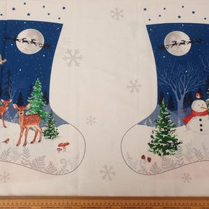 以下が含まれることがあります： クリスマスストッキングの生地。鹿、雪だるま、サンタのそりなど、冬のシーンが描かれています。濃い青色の夜空を背景にしています。ストッキングの上部は白で、青い星が描かれています。