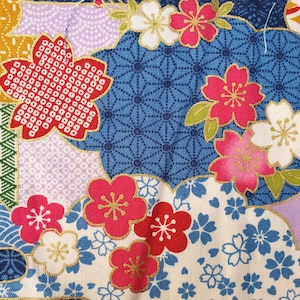 Puede incluir: Primer plano de una tela con un diseño floral japonés. La tela presenta flores rojas, rosas y blancas con detalles dorados sobre un fondo azul y crema. El diseño incluye patrones geométricos y formas de nubes.