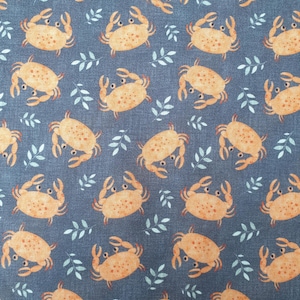 May include: A dark blue fabric featuring a repeating pattern of orange crabs with small dark spots and light blue leaf sprigs scattered between them. The crabs are depicted in a simple style with visible claws and eyes on a textured background.