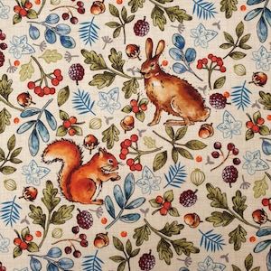 May include: A light beige fabric featuring a repeating pattern of brown rabbits, orange squirrels, dark purple blackberries, red berries, acorns, and green oak leaves. The design includes blue and green foliage accents on a subtle grid background.