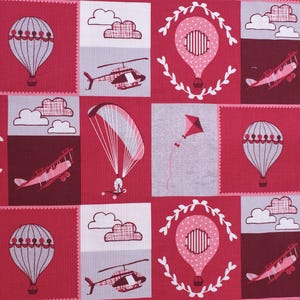 May include: A pink and white fabric with a repeating pattern of hot air balloons, airplanes, helicopters, parachutes, and clouds. The fabric has a patchwork design with squares and rectangles.