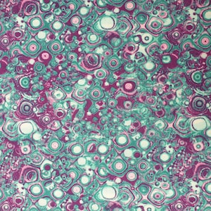 以下が含まれることがあります： ターコイズ、パープル、ホワイトの渦巻き模様の抽象的な生地。模様はマーブル模様に似ています。