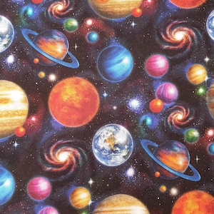 May include: A fabric print featuring a deep black space background filled with colourful planets, including ringed gas giants, Earth-like spheres, and swirling spiral galaxies. The design includes various shades of orange, blue, purple, and yellow.