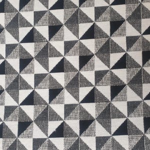 Może przedstawiać: Abstrakcyjny wzór geometryczny z powtarzającym się trójkątnym wzorem w kolorach czarnym, szarym i białym. Trójkąty ułożone są w siatkę, tworząc teksturowany, graficzny wzór. Projekt ma nowoczesną estetykę.