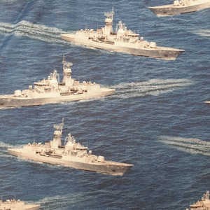 May include: A repeating pattern of gray naval ships sailing on a blue ocean. The ships are detailed with various structures and antennas. The water has white wave patterns.