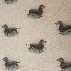 May include: A repeating pattern of black and tan dachshunds on a light beige background. The dachshunds are depicted in a realistic style, with detailed fur and features. The dogs are evenly spaced across the fabric.