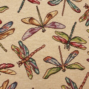 May include: A beige fabric with a repeating pattern of colorful dragonflies. The dragonflies have green, blue, red, and brown wings.