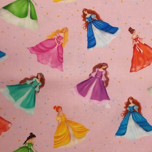 Puede incluir: Tela rosa con ilustraciones de princesas con vestidos coloridos. Las princesas tienen el pelo largo y están dispersas por la tela. La tela también tiene pequeños detalles de confeti.