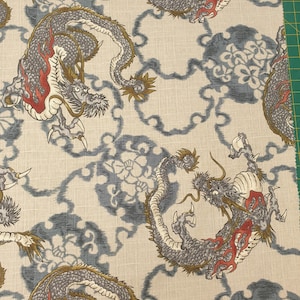 May include: A beige fabric featuring a repeating pattern of grey dragons with red accents and gold horns. The dragons are interspersed with blue circular floral motifs and a thin, wavy blue line pattern across the entire surface of the textile.