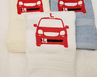 May include: Three white towels with red embroidered cars with an 'L' on the roof. The towels are stacked on top of each other. The bottom towel is light blue.