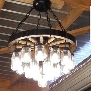 May include: A rustic wagon wheel chandelier with mason jar lights. The chandelier is made of wood and metal and has a distressed finish. The mason jars are clear glass and have Edison bulbs inside. The chandelier is hanging from a chain.