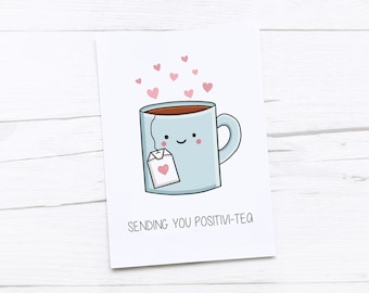May include: A white card with a blue mug with a smiling face and a tea bag with a heart on it. Pink hearts are floating above the mug. The text on the card reads "Sending you positivi-tea."