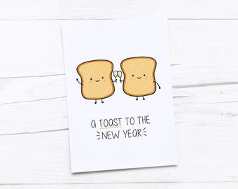 May include: A white greeting card featuring a cartoon illustration of two slices of toast, each with a smiling face. One toast slice holds two champagne flutes. The text "a toast to the new year" is below the toast characters.
