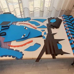 May include: A set of blue and black foam pieces for crafting a large toy truck. The pieces include wheels, tires, and body parts. The pieces are laid out on a table with the word "example" written on the table.