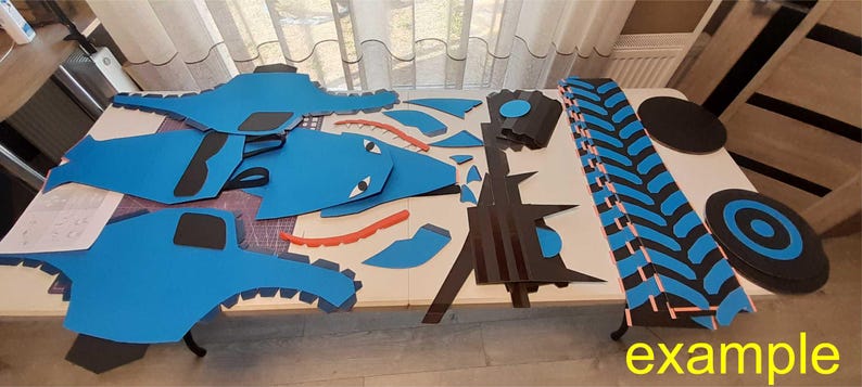 May include: A set of blue and black foam pieces for crafting a large toy truck. The pieces include wheels, tires, and body parts. The pieces are laid out on a table with the word "example" written on the table.