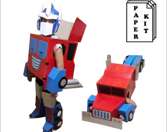 May include: A red, blue, and white paper kit costume resembling a robot. The costume includes a helmet, chest, arms, and legs. A second, similar robot truck is also shown. The text "PAPER KIT" is visible.
